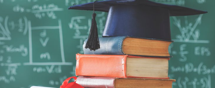 High School Diploma alternatives, graduate hat on top of a pile of books in front of a chalkboard